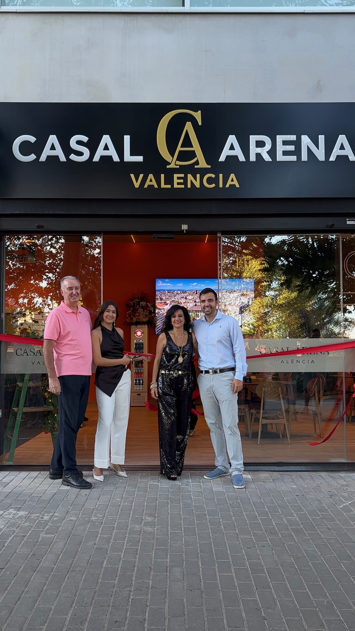 Corte de cinta en la inauguración de Casal Arena, frente al cartel del local